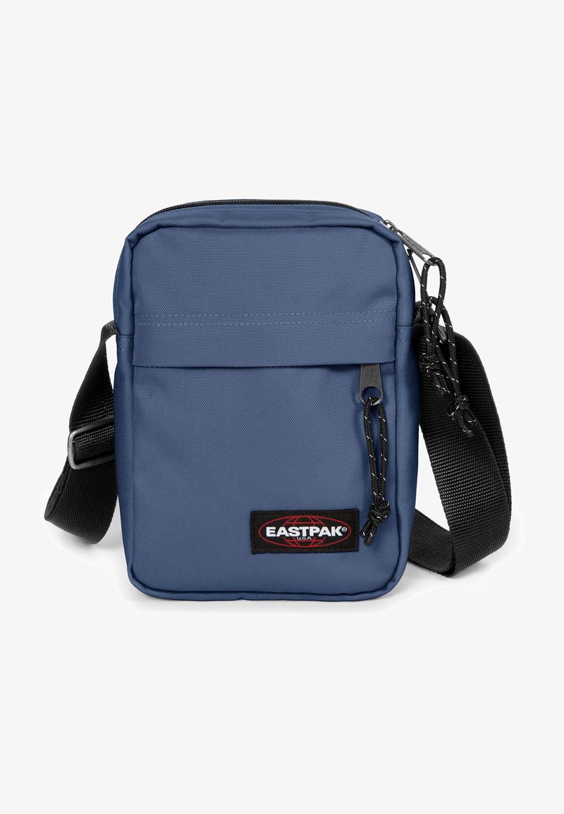 Borsa a tracolla blu in poliestere con chiusura a zip, tracolla regolabile, tasca frontale e patch con logo. Superficie testurizzata, forma rettangolare compatta.