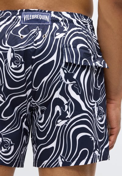 Jūras zils peldbaseins bikses ar baltu abstraktu viļņu rakstu un orku dizainu, elastīgu jostasvietu un sānu kabatu ar atloku.