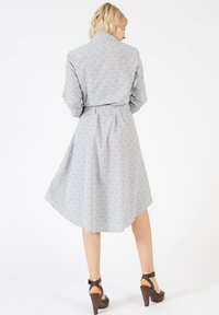 Robe bleu clair à motif, avec un col, des manches longues et une taille cintrée, s'évasant jusqu'à un ourlet mi-mollet, assortie à des talons marron.