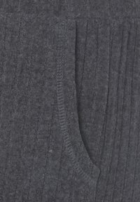 Tissu texturé gris foncé avec des motifs côtelés verticaux, incluant une poche latérale et une apparence douce et duveteuse. Les détails de couture sont visibles.