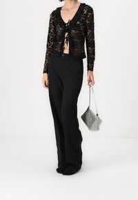 Top corto in pizzo nero con orli arricciati, caratterizzato da un profondo scollo a V e chiusura con laccetto. Abbinato a pantaloni neri a gamba larga e una borsa a tracolla argento.