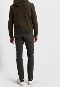 Sweat à capuche à motif camouflage foncé, associé à un pantalon slim vert foncé et des baskets blanches, vu de dos.