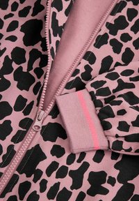 Różowa kurtka zapinana na zamek z czarnym nadrukiem w panterę. Posiada zamek błyskawiczny, ściągacze na rękawach i miękką teksturę. Podkreślona różowym paskiem na mankietach.