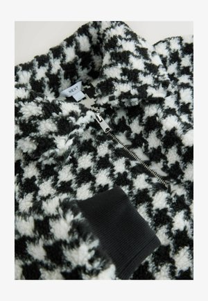 Svart och vit hounds-tooth zip-up fleece med en mjuk, strukturerad yta. Har svarta ribbade manschetter och en silverdragkedja. Varumärkesetikett synlig.