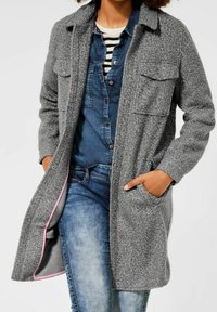 Cappotto di pile grigio con superficie testurizzata, tasche anteriori, chiusura a pulsante e rivestimento rosa a contrasto, indossato sopra una camicia di jeans.