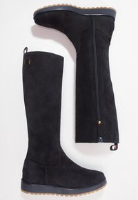 Botas altas de ante negras con cremallera lateral, punta redonda y suela de goma tan resistente; cuenta con un botón de marca y un tirador.