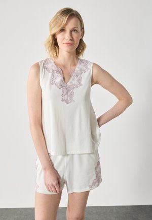 Top alb cu bretele lipsă și decolteu în V, cu un tiv din dantelă lila; asortat cu pantaloni scurți care au accente din dantelă lila.