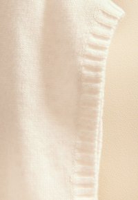 Suéter de lana crema con detalles acanalados en los hombros. Textura suave y diseño sin costuras, que destaca la simplicidad y la calidez.