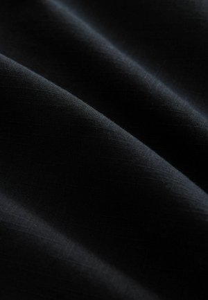 Tessuto nero con una superficie liscia, caratterizzato da morbide pieghe e una leggera lucentezza, che mostra una trama fine e senza motivi o accenti visibili.