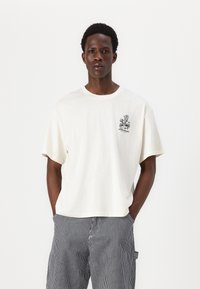 Camiseta de algodón blanca con cuello redondo, mangas cortas y un gráfico frontal que presenta un diseño floral en negro. Corte casual.