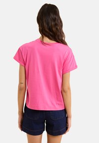 Camiseta de manga corta rosa con cuello redondo, material de algodón, corte relajado y mangas enrolladas, combinada con pantalones cortos de mezclilla oscura.