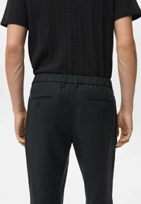 Pantalon noir avec une taille élastique, doté de deux poches arrière et d'une texture lisse, assorti à un haut noir côtelé.
