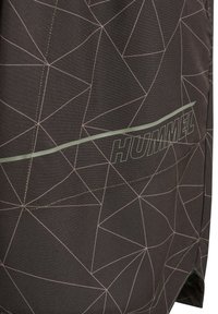 Posnetek temne tkanine s svetlim geometričnim vzorcem linij in odsevnim vodoravnim trakom nad logotipom "HUMMEL".