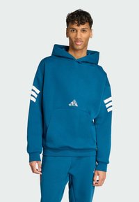 Blå hoodie i mjukt tyg, med en stor huva, framficka i kängurustil och vit tre-stripes-design på ärmarna.