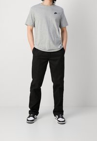 Šedé bavlněné tričko s černým logem Nike, spárované s volnými černými kalhotami a černo-bílými teniskami. Jednoduchý, neformální outfit.