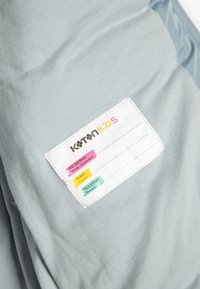 Tejido de color azul claro con una textura suave presenta una etiqueta blanca que muestra secciones coloridas para el nombre, la clase y los detalles del teléfono.