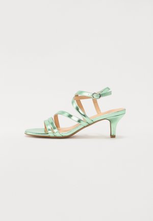 Grøn metalisk sandal med stropper, mellem-høj lille hæl og justerbar ankelrem på tan sål, set fra siden.