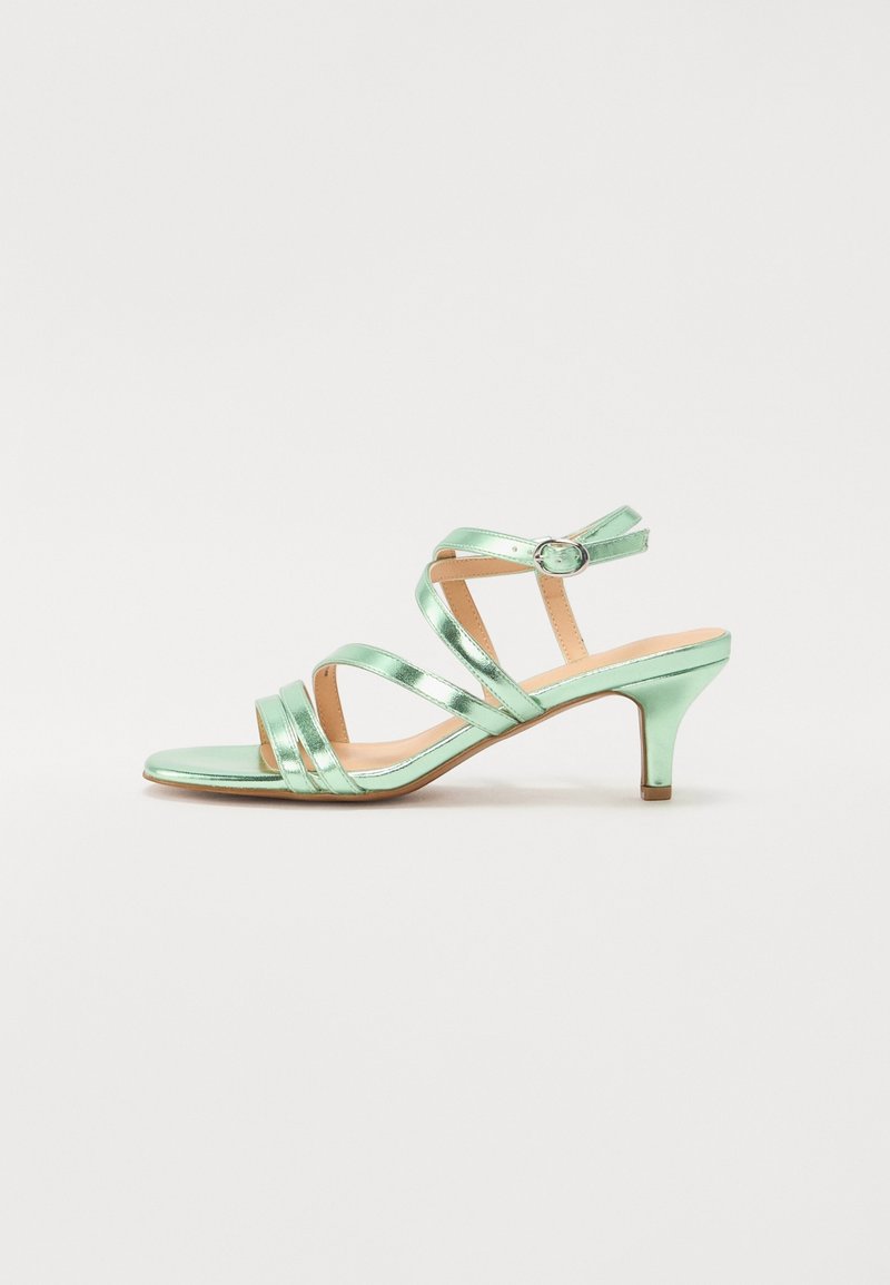 Sandale métallisée vert menthe à brides avec talon kitten de hauteur moyenne et boucle de cheville ajustable sur semelle couleur tan, vue de profil.