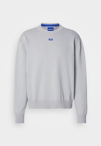 Pull gris clair à col rond avec poignets et ourlet côtelés, arborant un petit patch logo "HUGO" bleu sur la poitrine et à l'intérieur du col.