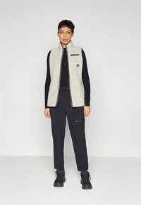 Flis prsluk svijetlosive boje s patentnim zatvaračem, džepovima i crnim detaljem. Upareno s tamnim cargo hlačama i crnom obućom.