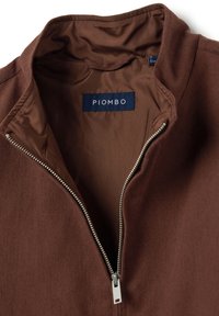 Braune Zip-Jacke mit glatter Stoffstruktur. Verfügt über einen silbernen Reißverschluss und ein blaues Etikett mit dem Markennamen "PIOMBO."
