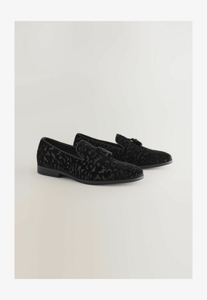 Schwarze Samtloafer mit strukturierter Oberfläche, ausgestattet mit einem dezenten Muster und einer kleinen Schleifenapplikation an der Seite. Flache Sohle, klassisches Design.