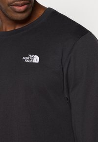 Μαύρο μακρυμάνικο T-shirt από βαμβάκι, με μικρό λευκό κεντημένο λογότυπο στο αριστερό στήθος. Λείο ύφασμα και στρογγυλή λαιμόκοψη.