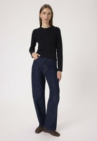 Black ribbed long-sleeve top paired with dark blue wide-leg jeans, featuring visible stitching and a relaxed silhouette. Brown ankle boots complete the outfit.