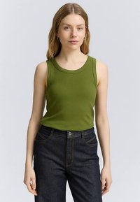 Zielony prążkowany top na ramiączkach z okrągłym dekoltem, w połączeniu z ciemnymi jeansami z klasycznym przeszyciem i zapięciem na guziki z przodu.