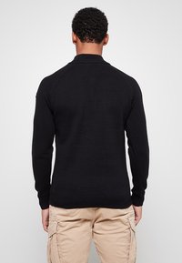 Czarny sweter z dzianiny z okrągłym dekoltem. Posiada rękawy raglanowe i ściągacze przy mankietach, prezentując gładką fakturę bez widocznych wzorów.