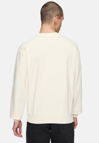 Sudadera de color crema con mangas largas, cuello redondo y ajuste relajado; tejido texturizado con puños y dobladillo acanalados.