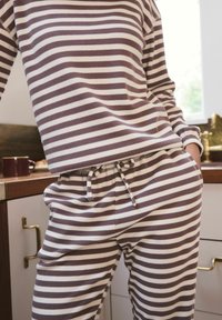Stribet loungewear-sæt i afdæmpet brune og hvide nuancer. Tekstureret stof med en afslappet pasform på toppen og bukser med snor i taljen, ideelt til komfort.