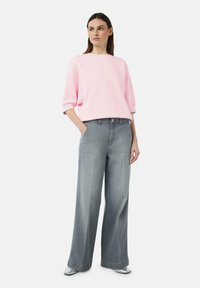 Helles rosa, übergroßes Sweatshirt mit Dreiviertelärmeln, kombiniert mit grauen, weiten Jeans. Dazu gehören silberne Schuhe; schlichtes Design und Farbpalette.