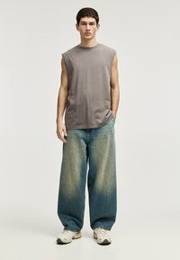 Hihaton harmaa puuvillapaita, leveät vaaleansiniset farkut, joissa on gradientsi viimeistely, ja valkoiset sneakerit. Minimalistinen muotoilu, rento istuvuus.