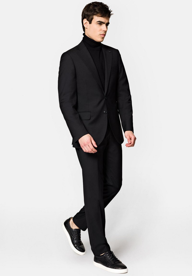 Czarny garnitur z dopasowaną marynarką i zwężanymi spodniami, połączony z czarnym golfem i teksturowanymi czarnymi sneakersami.