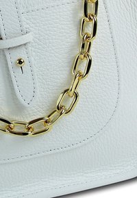 White leather bag featuring a textured surface, gold chain detail, and a front flap with a snap closure. Accented with contrasting stitching.