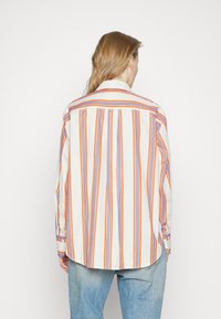 Långärmad skjorta i krämfärg med vertikala orange och blå ränder, med knapp-down krage och rundad nederkant. Lättviktsmaterial.