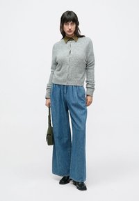 Γκρι πλεκτή ζακέτα με κουμπιά μπροστά, συνδυασμένη με μπλε τζιν παντελόνια φαρδιάς γραμμής. Μαύρα μποτάκια αστραγάλου και πράσινη τσάντα, απλό πουκάμισο με γιακά από κάτω.