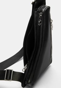 Borsa a tracolla nera in pelle sintetica con diverse tasche con zip, forma rettangolare piatta e tracolla in tessuto regolabile.