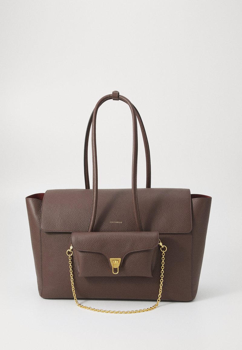 Sac en cuir marron avec deux longues anses, une surface texturée, et une petite poche avant avec une bandoulière en chaîne dorée et une fermeture à clip.