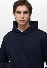 Mörkblå hoodie i ett mjukt tyg med en avslappnad passform. Har en minimalistisk design och smala, subtila sömmar längs sömmarna.