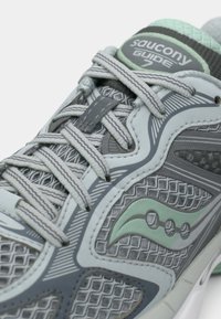 Γκρι αθλητικό παπούτσι με πλέγμα, με πράσινες λεπτομέρειες, υφασμάτινα επάνω μέρη και γκρι κορδόνια. Διακριτό λογότυπο στη γλώσσα και διακοσμητικά μοτίβα στα πλαϊνά.