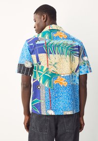 Chemise à manches courtes avec un imprimé graphique coloré aux éléments bleus, verts et orange, en tissu léger, avec une coupe décontractée.