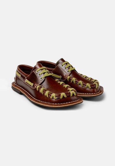 Scarpe in pelle marrone con lacci e cuciture verdi decorative. Presentano una punta arrotondata e una suola piatta, con un design elegante e occhielli per i lacci.