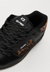 Black skate shoes with suede and leopard print accents. Features black laces, a padded collar, and a prominent logo on the tongue.