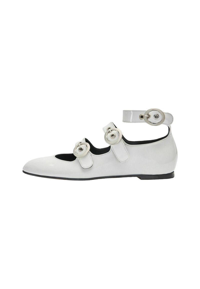 Zapato plano de charol blanco con tres hebillas redondas decorativas, tira en el tobillo y un tacón bajo. Presenta punta redondeada y un interior negro en contraste.