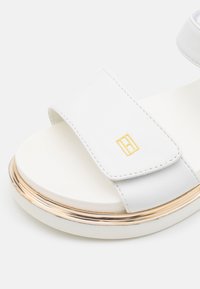 Białe sandały ze gładkim skórzanym paskiem i złotym akcentem wokół masywnej podeszwy. Posiadają miękką wkładkę dla wygody. Złoty detal z logo.