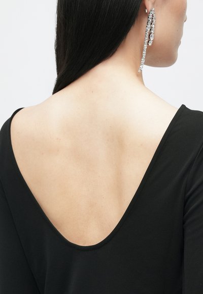 Top preto com um design V profundo nas costas, apresentando um tecido suave. Brincos longos e cintilantes caem ao lado do pescoço e do ombro.