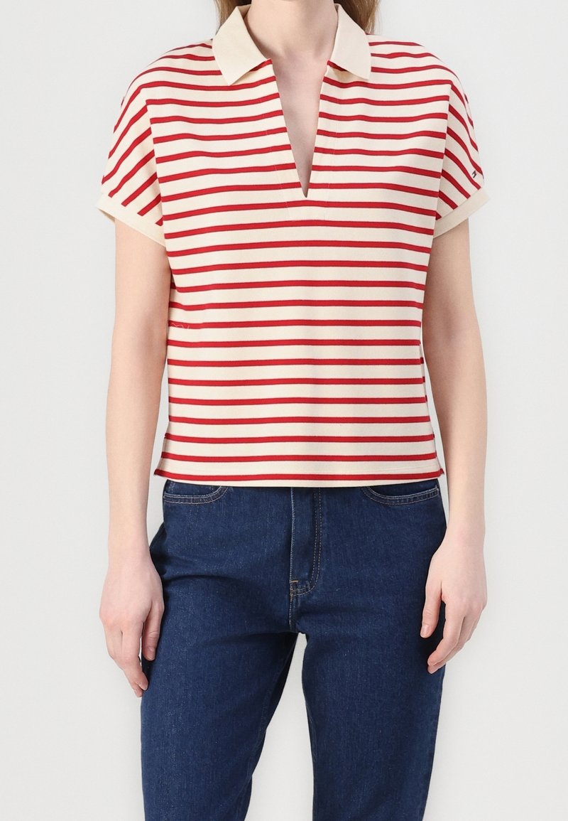 Červeno-krémový proužkovaný polo tričko s krátkým rukávem a V- výstřihem, kontrastním límcem a volným střihem, spárované s tmavě modrými džínami.