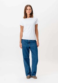 Hvid bomulds t-shirt med korte ærmer, parret med blå lige ben jeans. Outfitet har en afslappet pasform og en casual design.